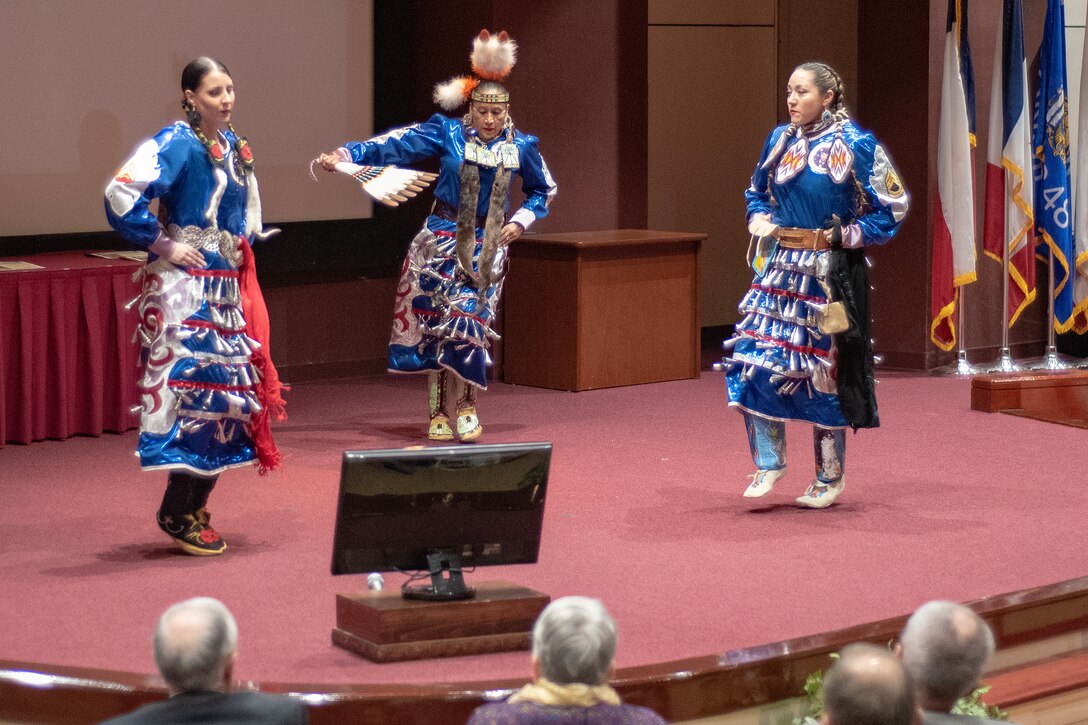 Three members of the Native American Women Warriors perform a tribal dance for attendees of the National American Indian Heritage Month observance at Redstone Arsenal, Alabama, Nov. 13, 2019. Pictured are Army veteran Keshon Smith, right; Marine Corps veteran Carrie Lewis, left; and Army veteran Mitchelene BigMan, center, president and founder of NAWW. The observance was organized by Huntsville Center’s Equal Employment Opportunity office in coordination with Team Redstone and the U.S. Army Aviation and Missile Command. The Native American Women Warriors are an all-female group of Native American veterans who started as a color guard but have since grown and branched out as advocates for Native American women veterans in areas such as health, education and employment. The members make appearances at various events around the country, serving as motivational and keynote speakers, performing tribal dances, and fulfilling the role of color guard representing all branches of the U.S. military.