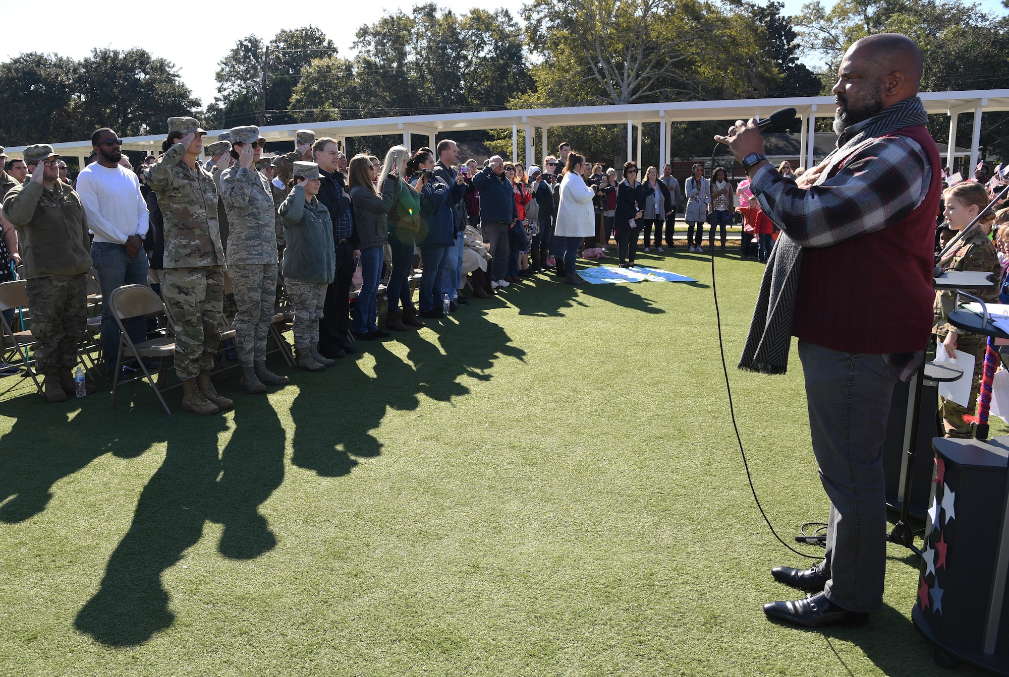 Keesler Air Force Base personnel and family members pay their respects during the singing of the national anthem by U.S. Navy veteran Bryant White during the Jeff Davis Elementary School Veterans Day celebration in Biloxi, Mississippi, Nov. 15, 2019. During the event, students also recited the Pledge of Allegiance. Keesler Air Force Base leadership and base personnel attended the event. (U.S. Air Force photo by Kemberly Groue)