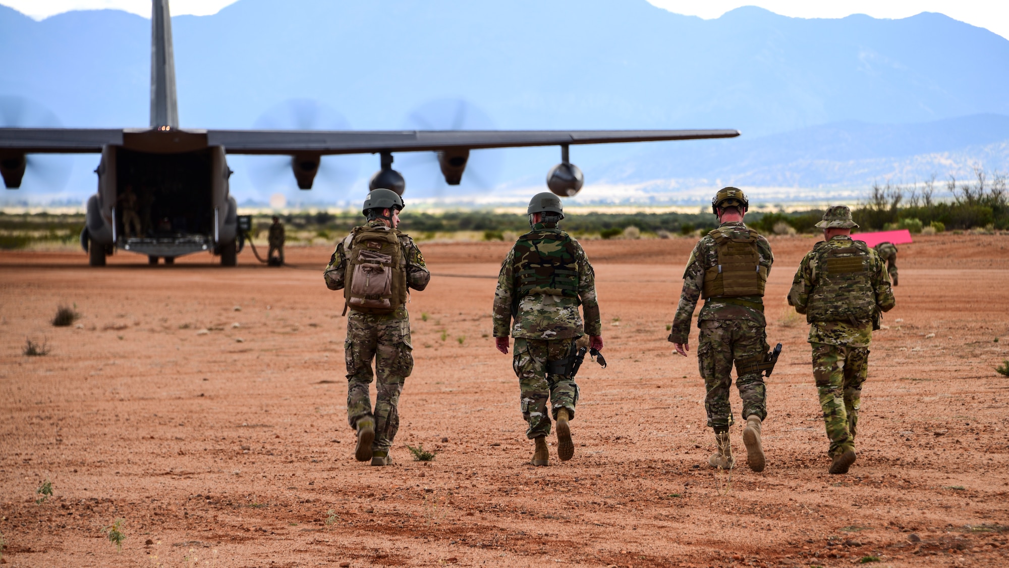 A photo of four airmen walking towards an HC-130J on a dirt runway.
