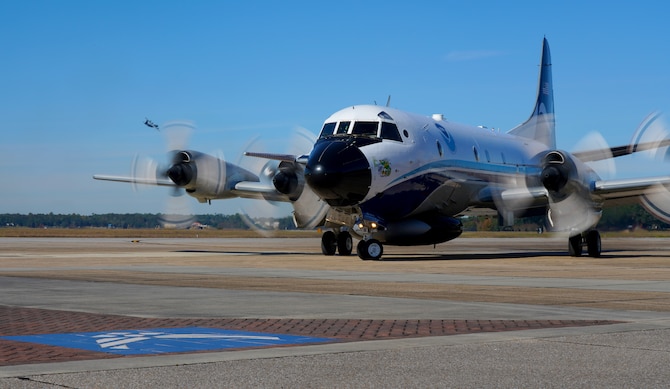 A National Oceanic and Atmospheric Administration Aircraft Operations Center WP-3D Orion aircraft prepares to park on the flightline, as a 53rd Weather Reconnaissance Squadron WC-130J Super Hercules flies in the background at Keesler Air Force Base, Miss., Nov. 13, 2019. Both teams of Hurricane Hunters met to share information and review the 2019 hurricane season. (U.S. Air Force photo by Senior Airman Kristen Pittman)