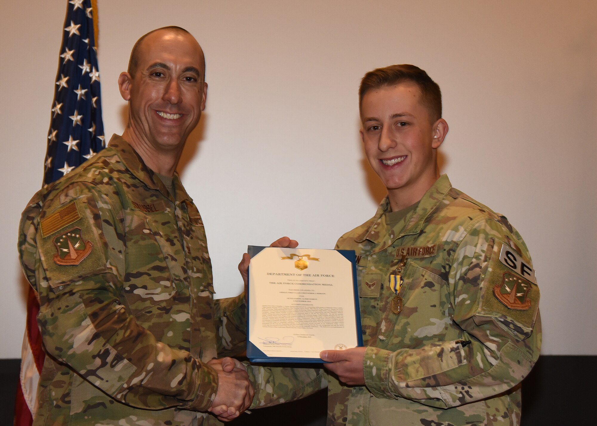 Airman 1st Class Christopher Horton, 790th MSFS Defender, receives an Air Force Commendation Award from 90th Security Forces Group Commander Col. Damian Schlussel during a ceremony Nov. 15, 2019, at the Base Theater on F. E. Warren Air Force Base, Wyo. Horton received the commendation for actions taken in rescuing a family in danger of a house fire Nov. 7 in Dix, Nebraska. Horton was recognized alongside his teammate, Airman 1st Class Christian Reid. (Air Force photo by Glenn S. Robertson)