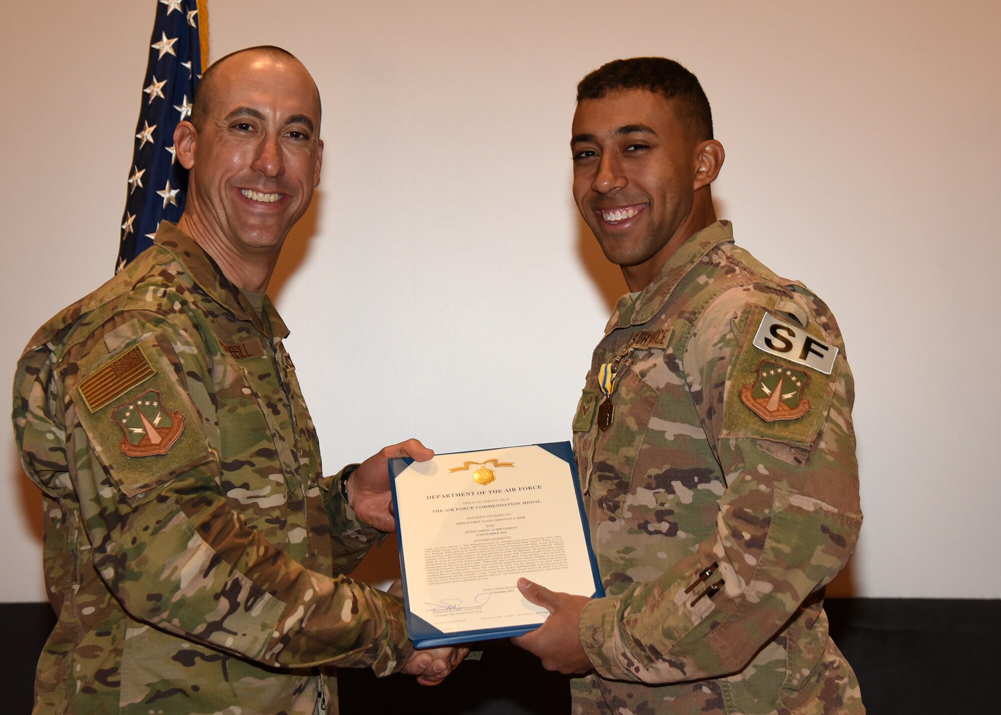 Airman 1st Class Christian Reid, 790th MSFS Defender, receives an Air Force Commendation Award from 90th Security Forces Group Commander Col. Damian Schlussel during a ceremony Nov. 15, 2019, at the Base Theater on F. E. Warren Air Force Base, Wyo. Horton received the commendation for actions taken in rescuing a family in danger of a house fire Nov. 7 in Dix, Nebraska. Reid was recognized alongside his teammate, Airman 1st Class Christopher Horton. (Air Force photo by Glenn S. Robertson)