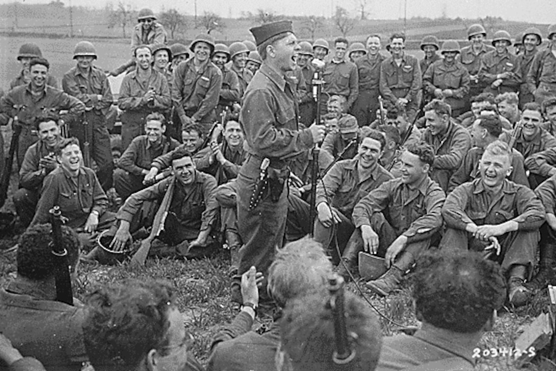 A single man stands amidst an audience of dozens of soldiers.