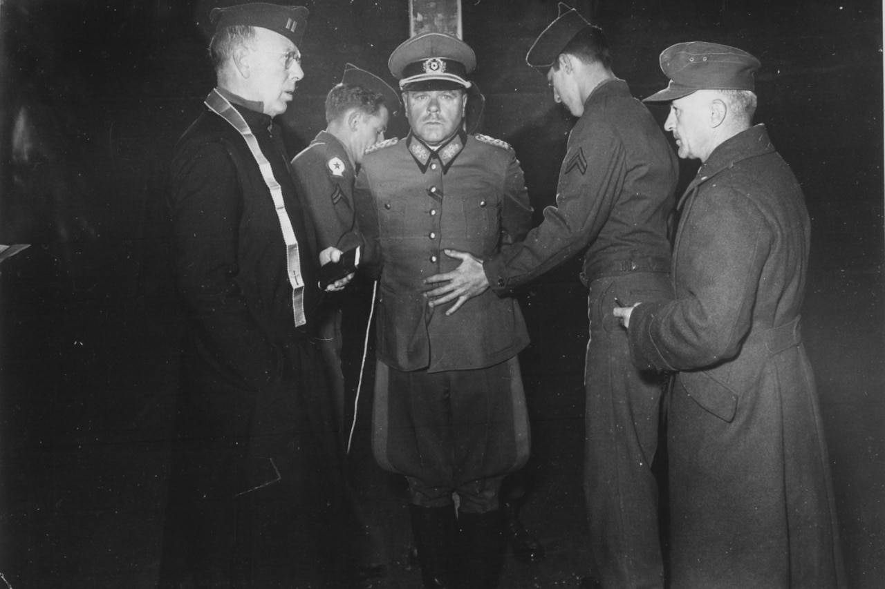 Four men surround another, who is tied to a wooden stake.