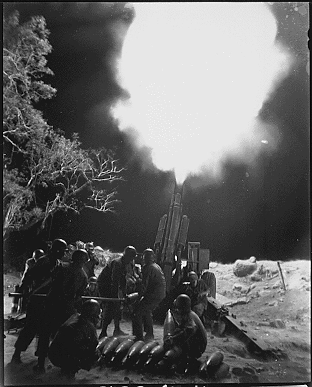 Soldiers fire heavy artillery at night.