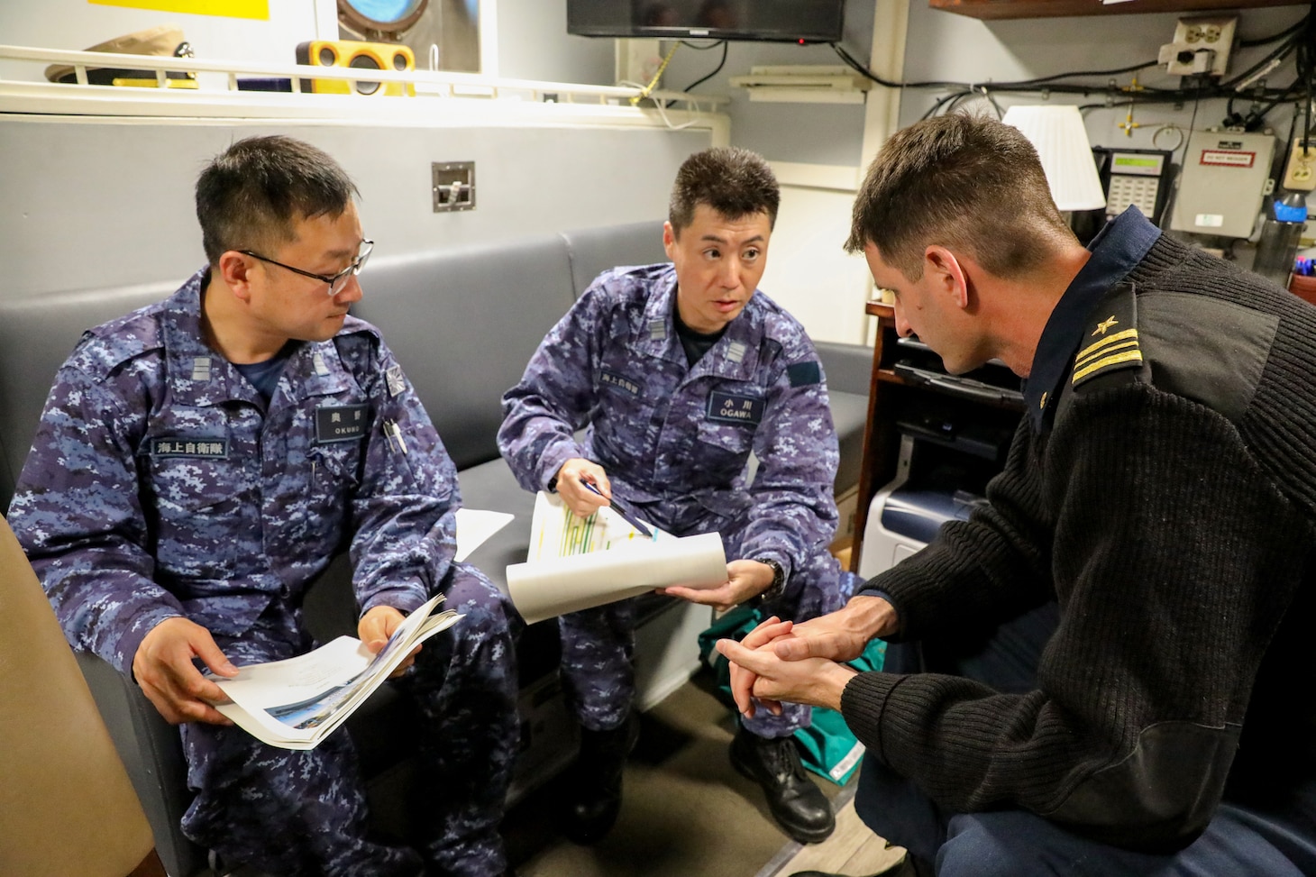 Commanding officer of Avenger-class mine countermeasures ship USS Pioneer (MCM 9)  Lt. Cmdr. Bobby Wayland, right, discusses upcoming operations for Mine Warfare Exercise 3JA 2019 with commanding officer of Japanese mine countermeasure ship JS Hirashima (MSC 601), Lt. Cmdr. Ogawa Tomoyuki, middle, and Commander of the route survey division for JMSDF Mine Warfare Support Center, Lt. Cmdr. Okuno Kazuyuki.