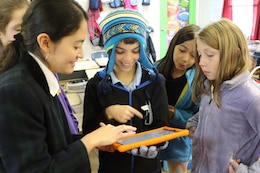 Scientist from Norfolk District holds mobile tablet and explais to smiling children how to work the application