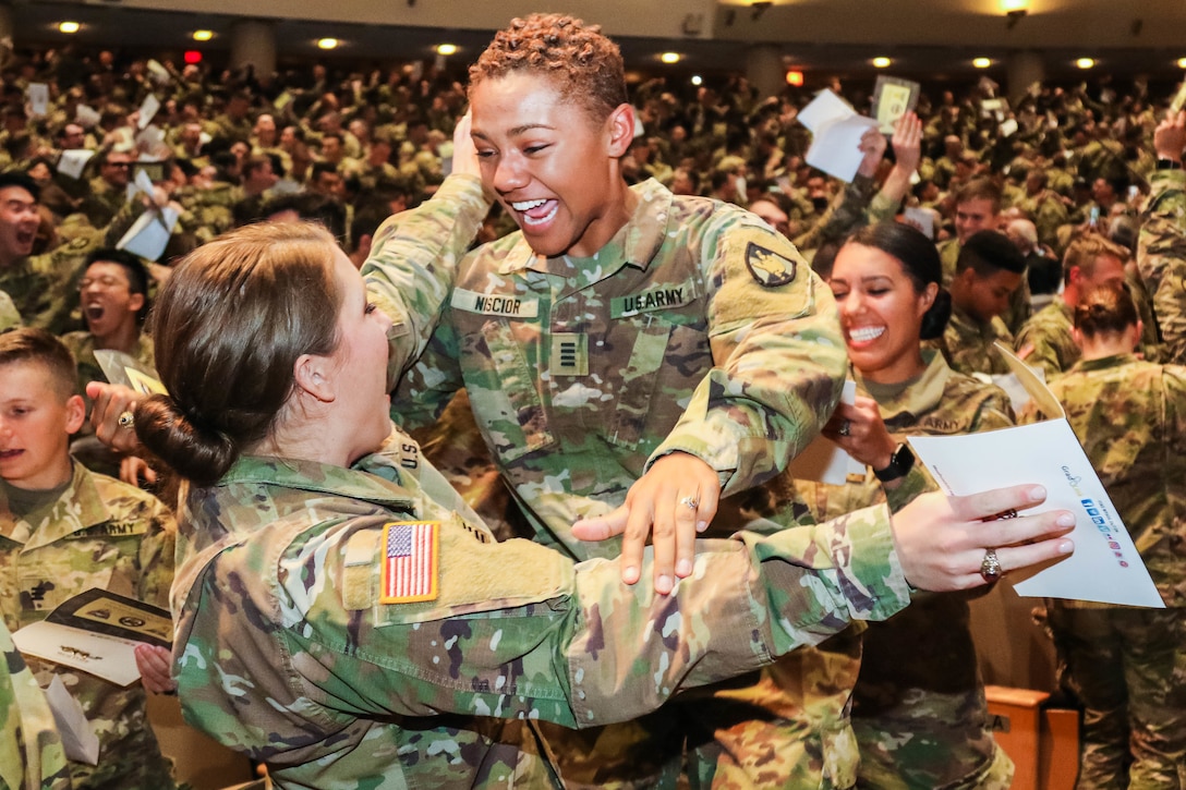 Two Army cadets laugh and embrace at a ceremony.