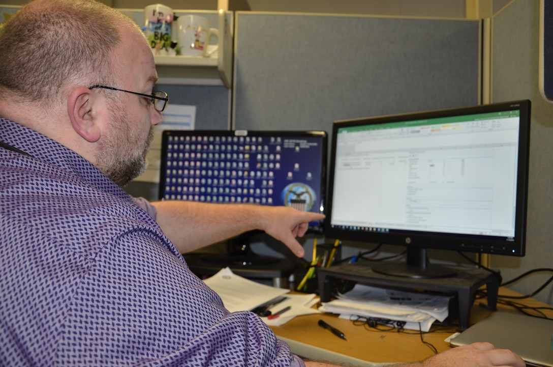 Bryan Mattheis, a systems accountant for business analysis and integration with DLA Finance at DLA Disposition Services, shows a colleague how he uses his spreadsheet system to study inventory data and look for errors that need correction.