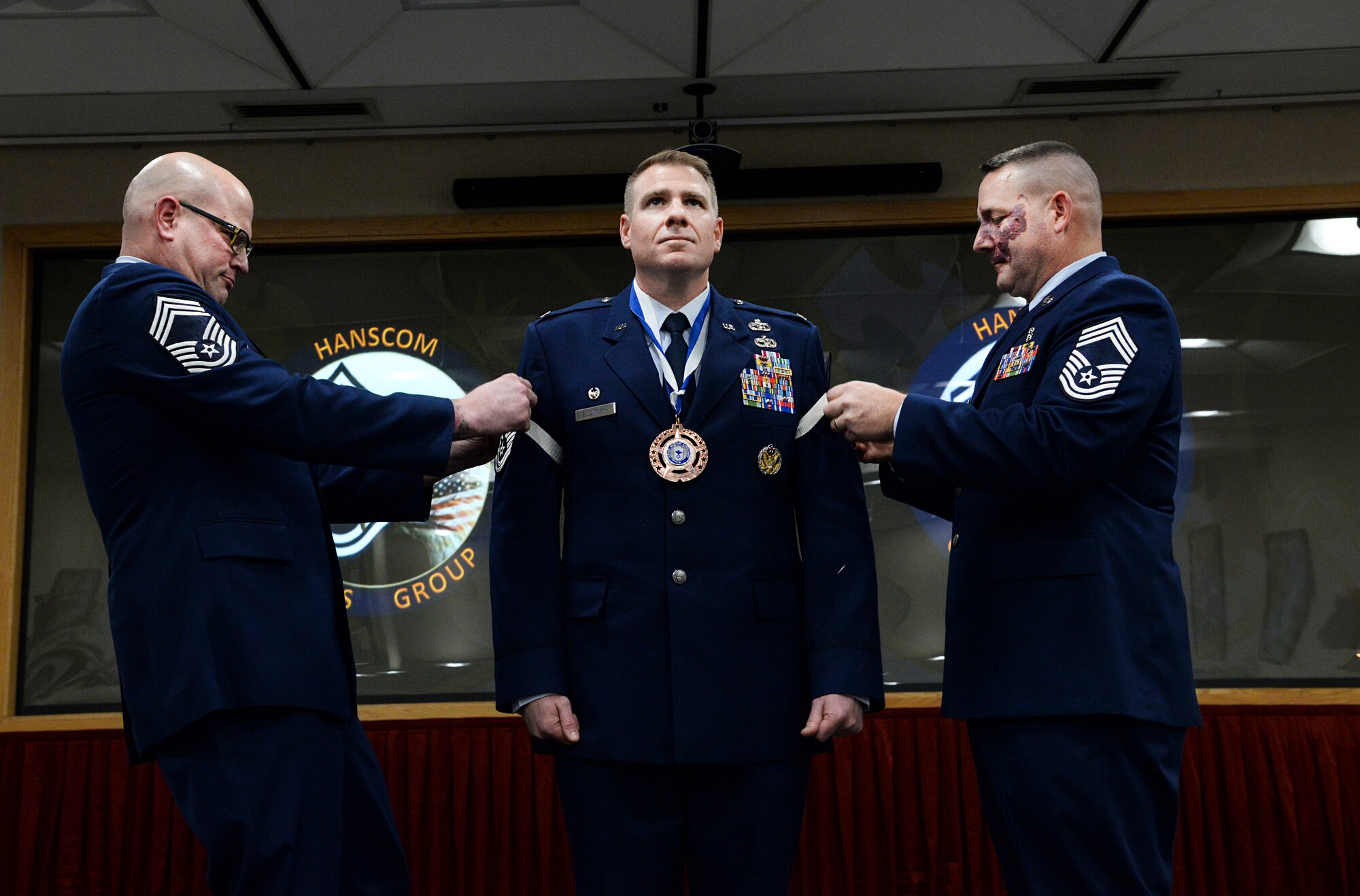 Chief Master Sgts. Michael Daly (left), 66th Security Forces Squadron manager, and Adam Page, 66th Medical Squadron superintendent, prepare to pin chief stripes on Col. Chad Ellsworth, 66th Air Base Group and installation commander, during an honorary chief induction ceremony on Hanscom Air Force Base, Mass., Nov. 15. Ellsworth is only the fourth 66th Air Base Group commander to receive the honor. (U.S. Air Force photo by Lauren Russell)