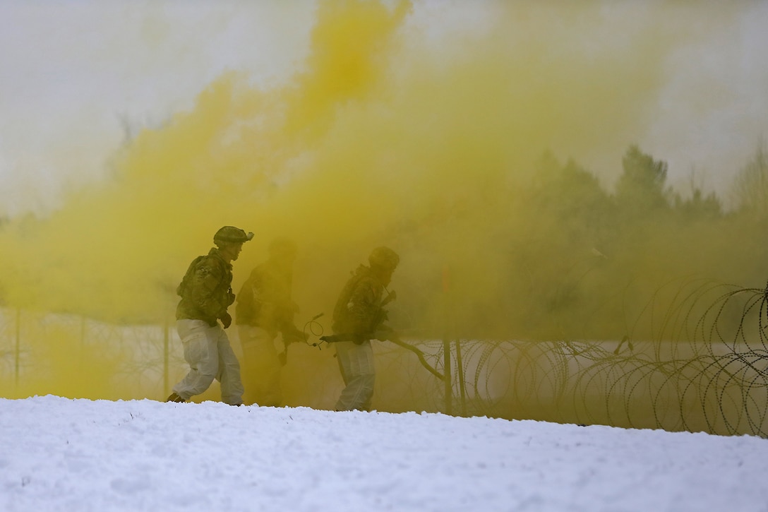 Two soldiers surrounded by yellow smoke  place explosives  in the snow.