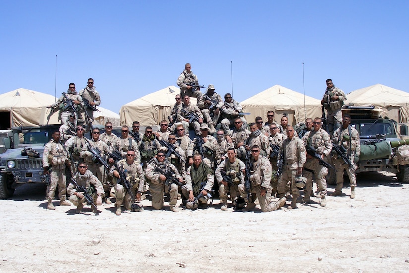 An Army platoon poses near two utility vehicles and a few tents in Afghanistan.