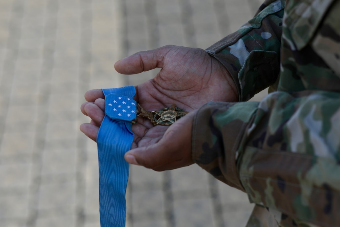 The Medal of Honor is held in the hands of a soldier in long-sleeve uniform.