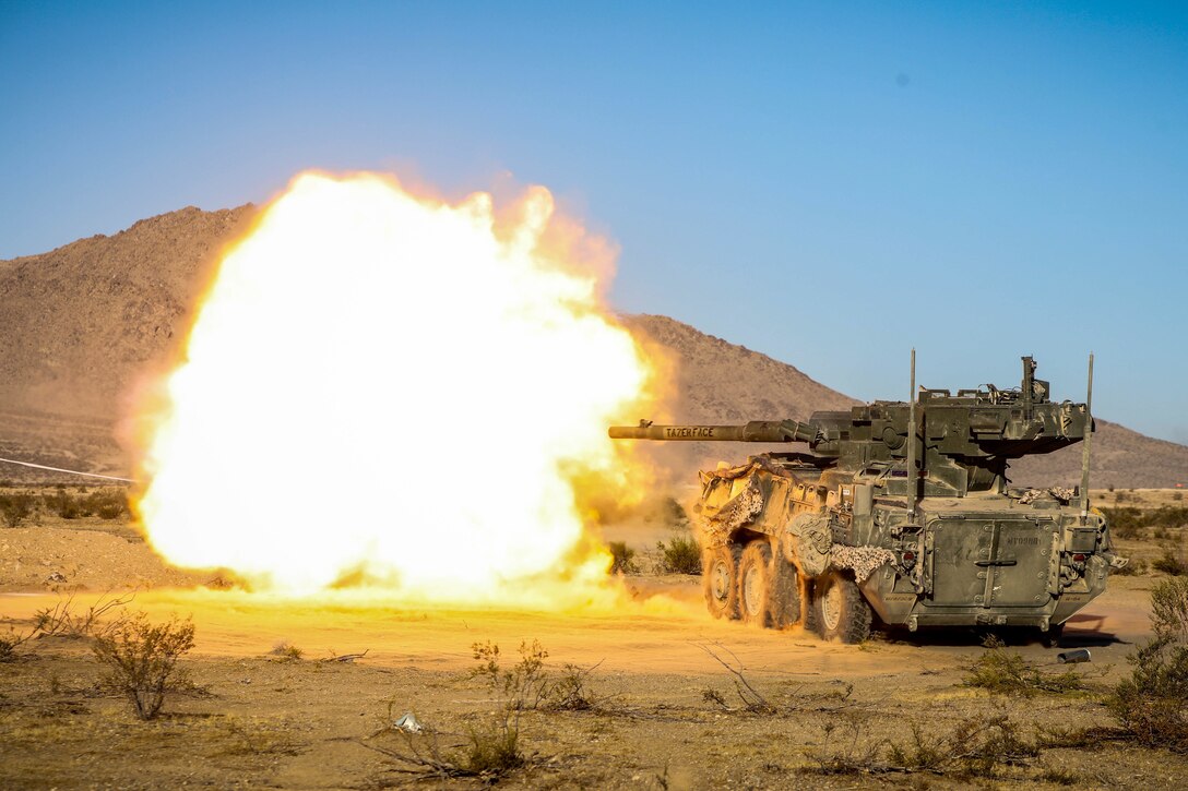 An M1128 Stryker Mobile Gun System fires, creating a massive fireball.