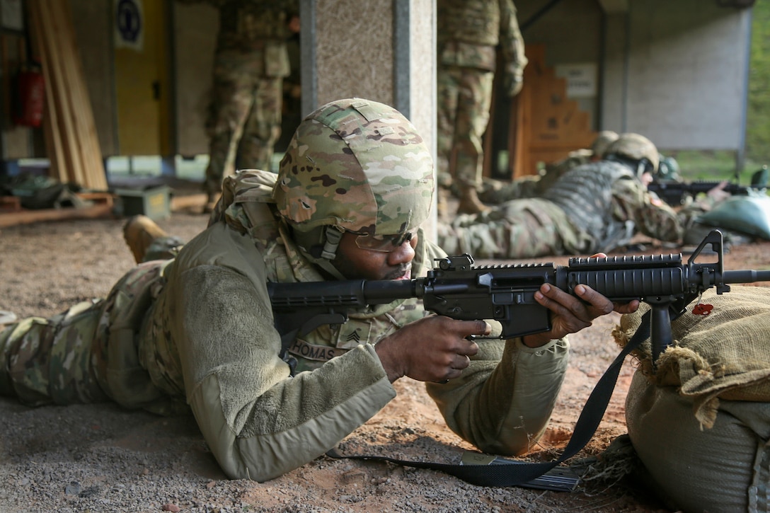 Soldiers in the prone position at a firing range aim weapons.