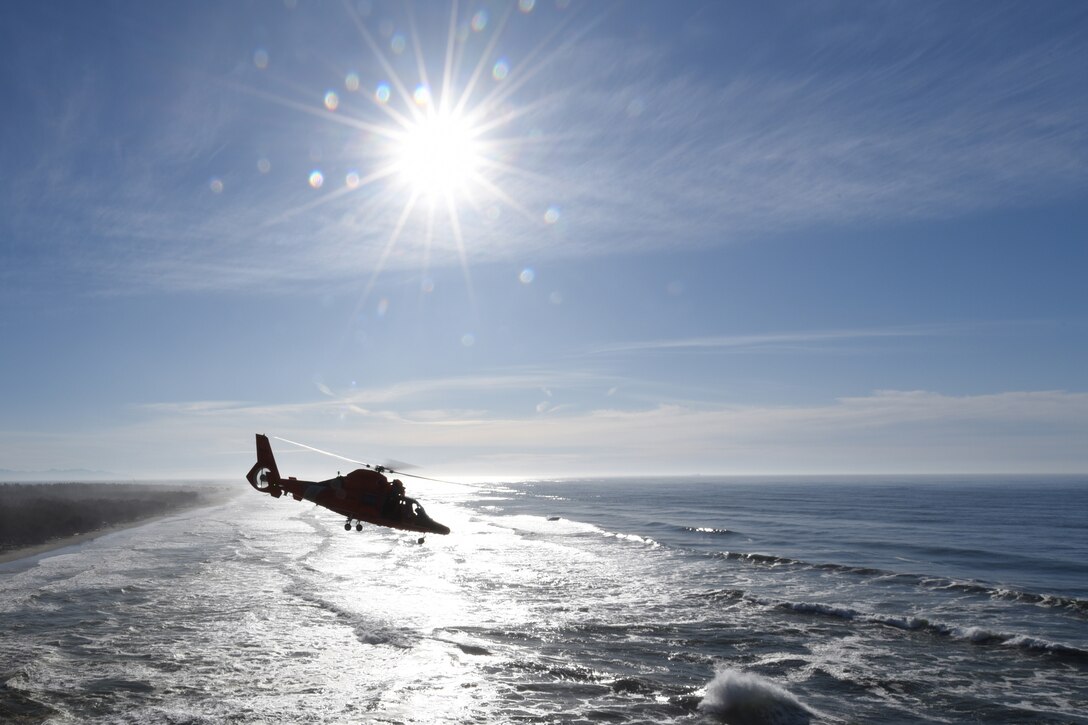 A helicopter flies low over the water in bright sunlight.