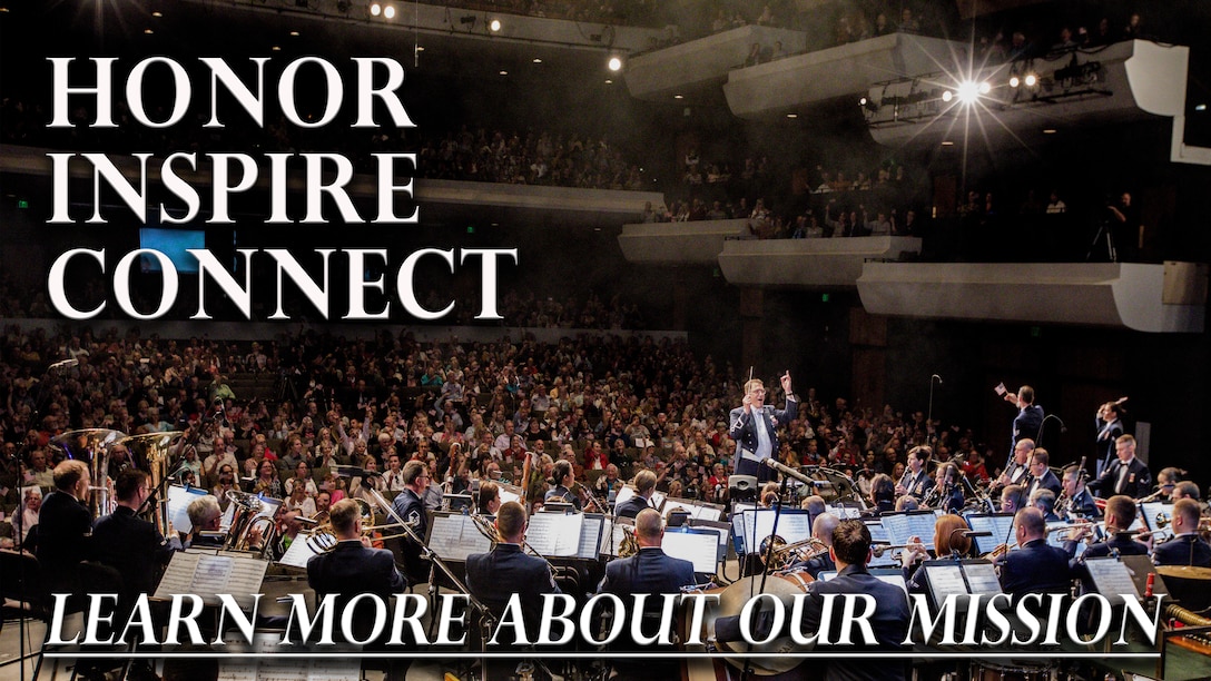 A Concert Band performs in an auditorium packed with people in patriotic garb, featuring vocalists reaching out to the audience and smoke from stage effects lingering in the air.