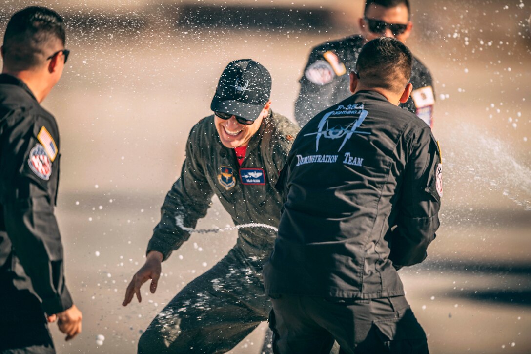 An airman smiles and braces himself as fellow teammates douse him with liquid on a flightline.