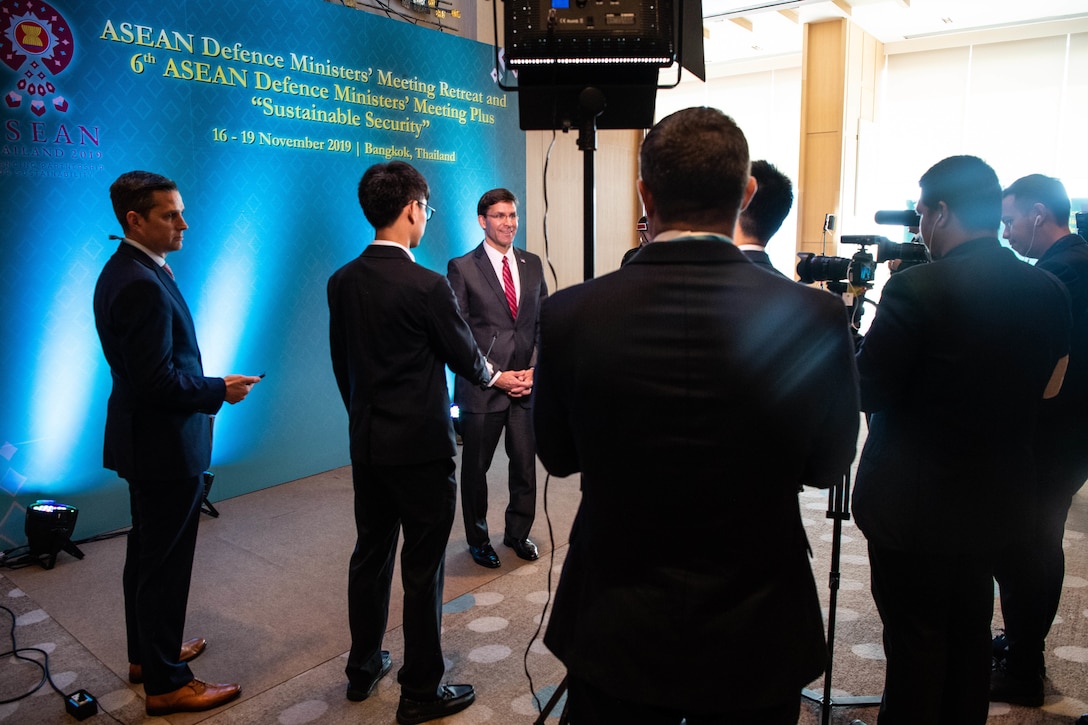 Defense Secretary Dr. Mark T. Esper stands and smiles in front of people with cameras.