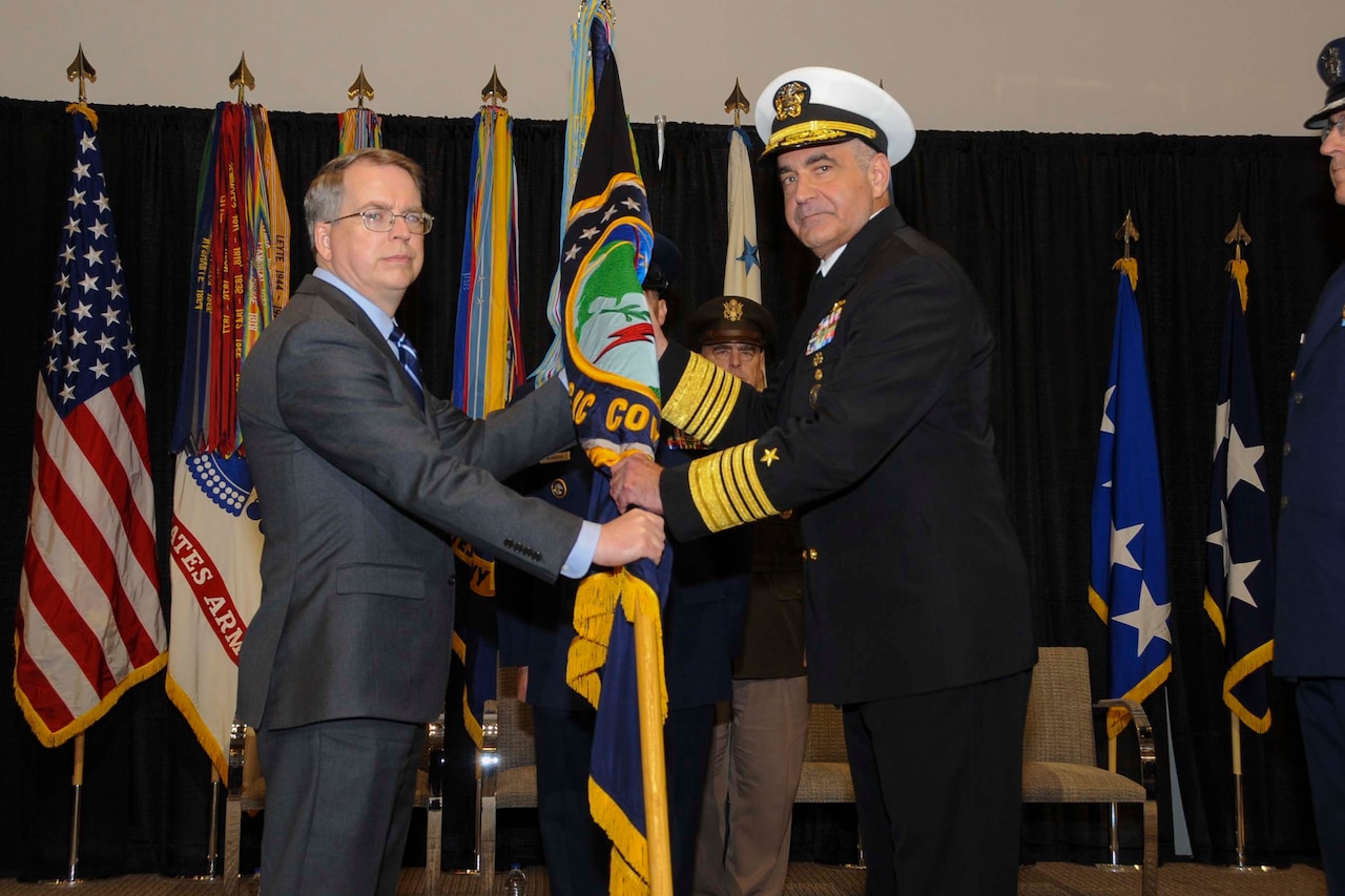 Deputy Defense Secretary David L. Norquist and Navy Adm. Charles A. Richard hold onto a flag together.