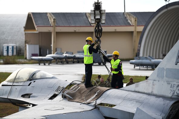 U.S. Airmen from the 31st Maintenance Squadron unhook a F-16 Fighting Falcon from the lifting sling attached to a 60 ton crane at Aviano Air Base, Italy, Nov. 16, 2019. The lifting sling and guide ropes were used to keep the F-16 stable during the lift. (U.S. Air Force photo by Airman 1st Class Ericka A. Woolever).