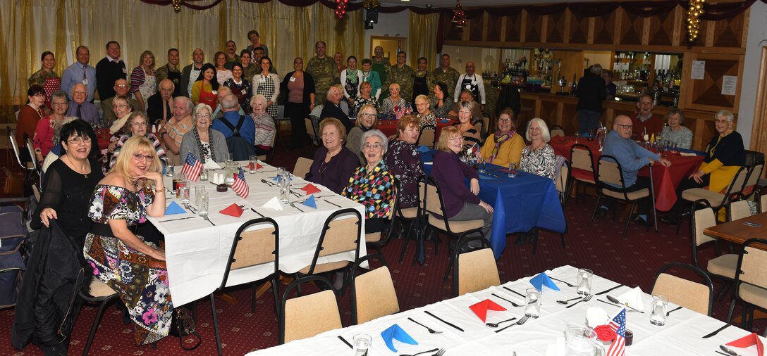 Volunteers from Team Mildenhall and its British-American Committee pose for a photo with senior citizens in the local community at the Mildenhall Social Club, Mildenhall, England, Nov. 18, 2019. Base leadership, Airmen and BAC members served the luncheon to build relations and give back to the local community. (U.S. Air Force photo by Karen Abeyasekere)
