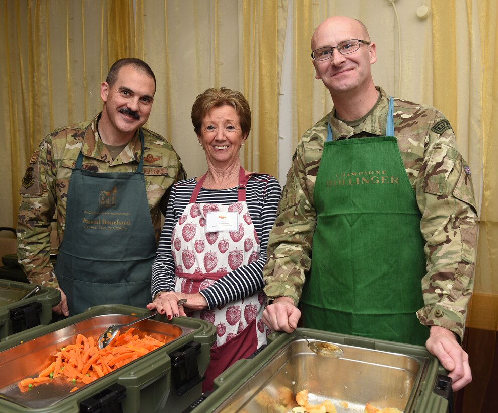 Colonel Robert Shelton, 100th Operations Group commander; Carol Thompson, British-American Committee member, and Sqdn. Ldr. Paul Graham, RAF Commander, RAFMildenhall, pose for a photo as they prepare to serve food at a Thanksgiving lunch for local senior citizens at the Mildenhall Social Club, Mildenhall, England, Nov. 18, 2019. Leadership, Airmen and BAC members from RAF Mildenhall served the luncheon to build relations and give back to the local community. (U.S. Air Force photo by Karen Abeyasekere)