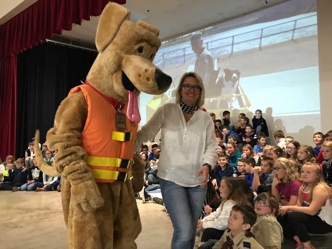 Cleveland, Okla., Intermediate School music and art teacher, Anja Johnson, introduces Bobber, the U.S. Army water safety dog, to school children as part of their annual Veterans Day recognition ceremony. Bobber helped pay tribute to veterans in the audience and also provided each child in attendance a grab-bag of water safety supplies and informational brochures.