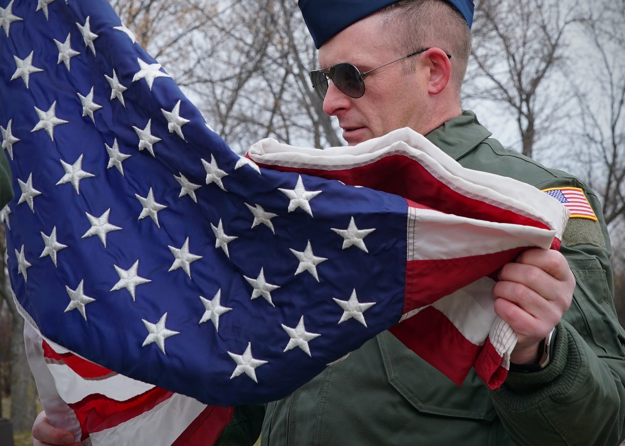 Master Sgt. Justin Baier, 348th Reconnaissance Squadron remotely piloted aircraft pilot trainee, unfolds a United States flag in preparation to be raised Nov. 8, 2019, on Grand Forks Air Force Base, North Dakota. Baier and other volunteers from the 348 RS spent a portion of their morning lowering state flags near the front of the installation in order to replace them with U.S. flags for Veterans Day. (U.S. Air Force photo by Senior Airman Elora J. Martinez)