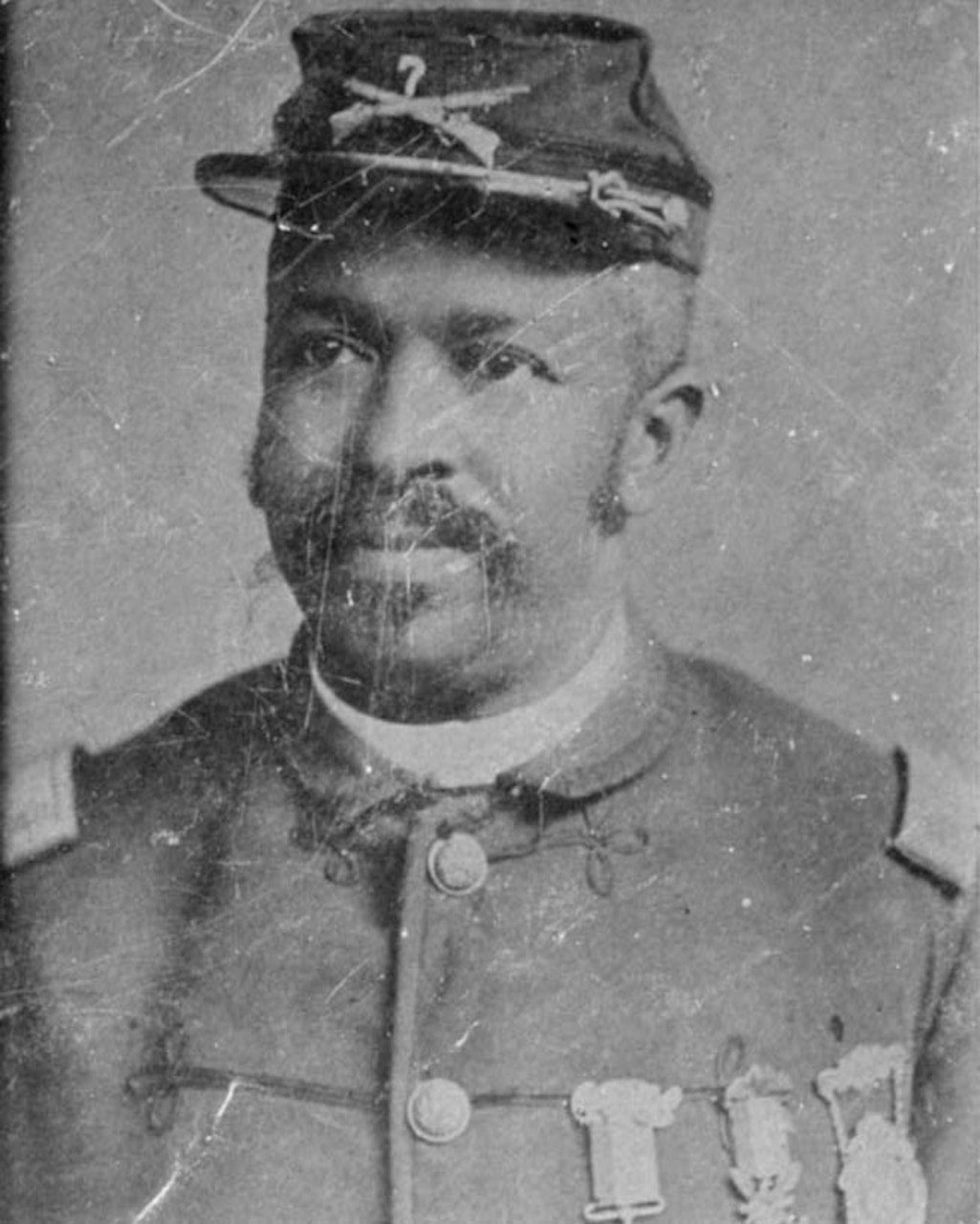 A black Civil War soldier wears his cap and uniform with three medals pinned to his dress shirt.