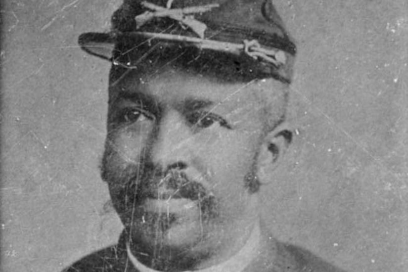 A black Civil War soldier wears his cap and uniform with three medals pinned to his dress shirt.