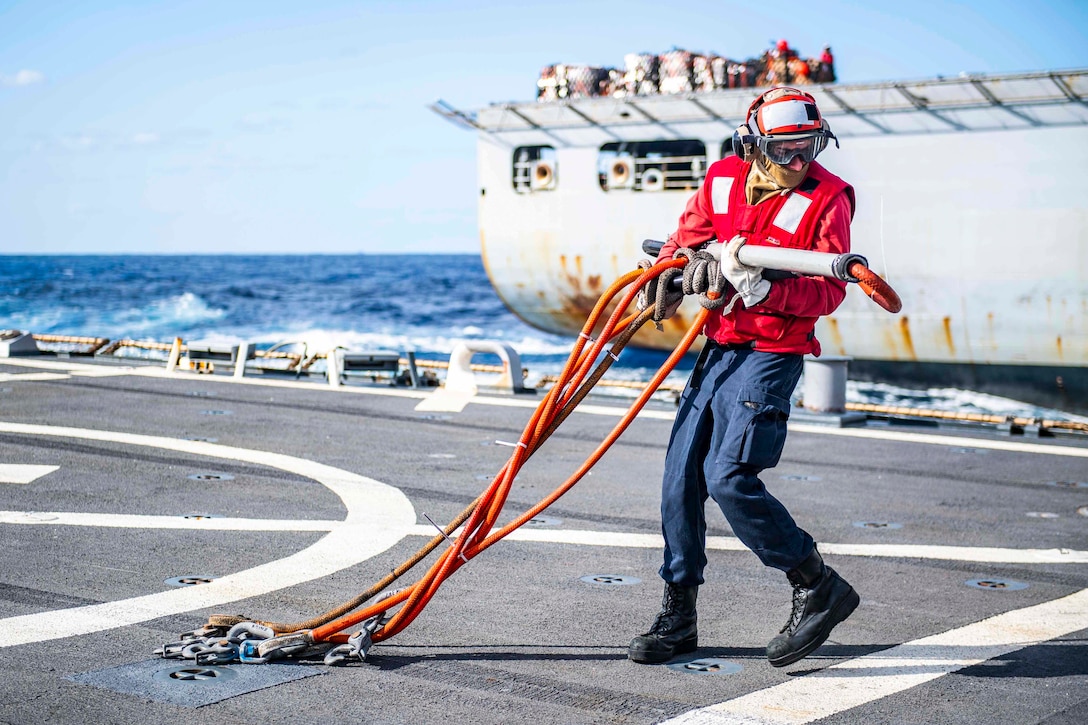 A sailor carries a hook across a ship's deck.