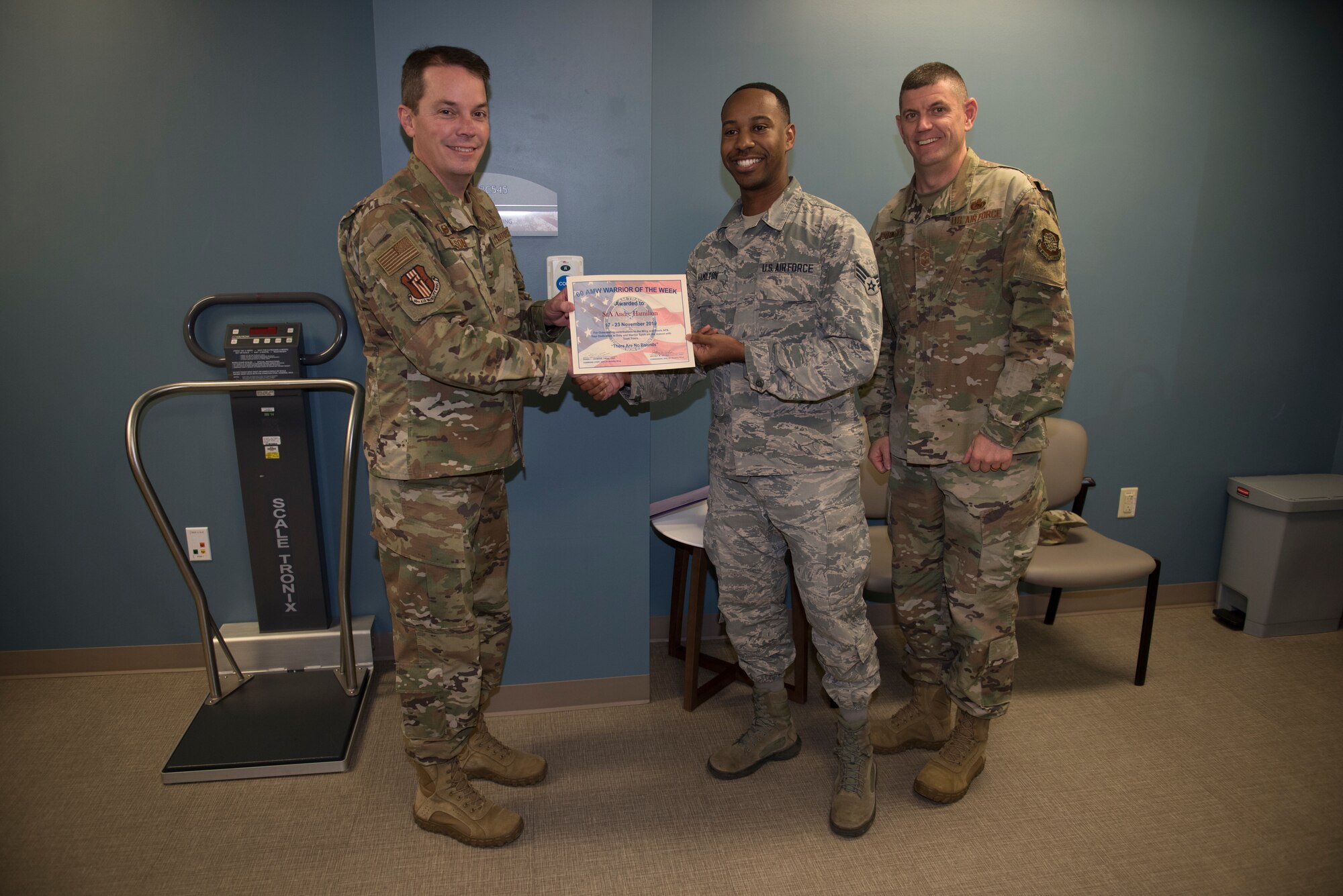U.S. Air Force Senior Airman Andre Hamilton, center, 60th Medical Support Squadron health services management technician, is recognized by Col. Jeffrey Nelson, left, 60th Air Mobility Wing commander, and Chief Master Sgt. Derek Crowder, right, 60th AMW command chief, as Warrior of the Week Nov. 19, 2019, at Travis Air Force Base, California. Hamilton was recognized as the WoW for Nov. 17-23. The program highlights a Travis Airman for his or her outstanding performance. (U.S. Air Force photo by Airman 1st Class Cameron Otte)