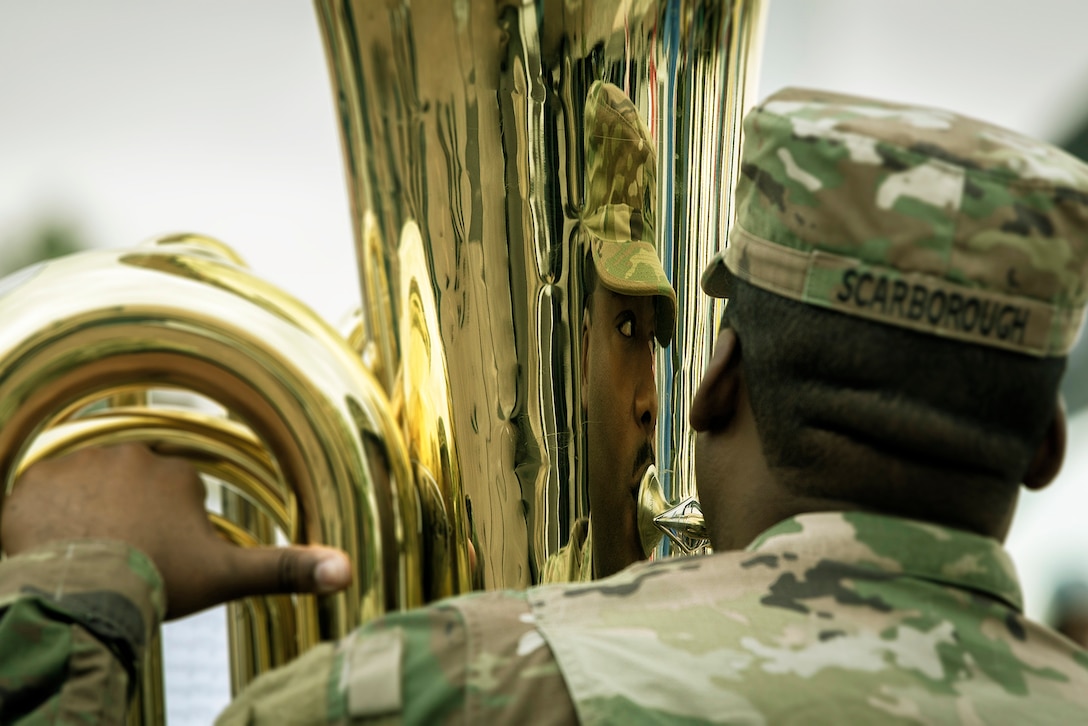 A soldier is reflected in the brass instrument he is playing.