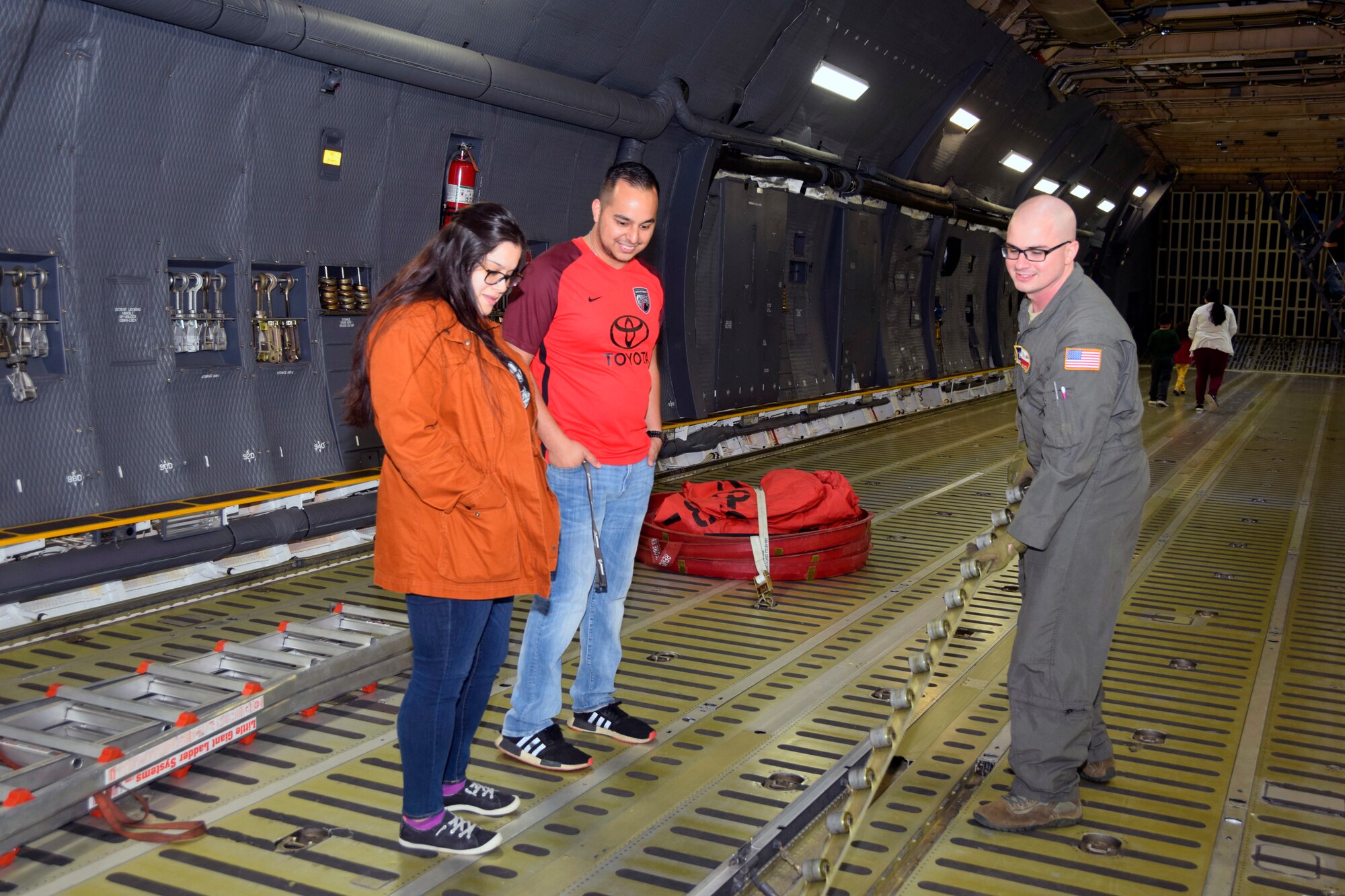 U.S. Air Force Staff Sgt. Michael L. Indo, 68th Airlift Squadron flight engineer, shows Ashley M. Jones and Kevin C. Castillo the inboard logistical rail and roller conveyer while inside a C-5M Super Galaxy aircraft during the Youth Aerospace Expo at Kelly Field, Texas, Nov. 16, 2019.