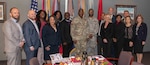 15 people stand in front of a set of organizational flags.