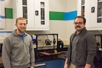 Jacob Aljundi (left) and Ryan Fisher, engineers in the Additive Manufacturing Branch at Naval Surface Warfare Center Carderock Division, stand in front of a 3D printer in Carderock’s Manufacturing, Knowledge and Education Lab on Nov. 15, 2019, in West Bethesda, Md. The two engineers travel to different parts of the world training deployed U.S. Marines how to use 3D printers and the associated software and technology. (U.S. Navy photo by Edvin Hernandez/Released)