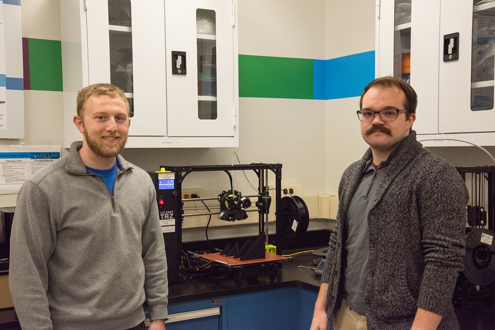 Jacob Aljundi (left) and Ryan Fisher, engineers in the Additive Manufacturing Branch at Naval Surface Warfare Center Carderock Division, stand in front of a 3D printer in Carderock’s Manufacturing, Knowledge and Education Lab on Nov. 15, 2019, in West Bethesda, Md. The two engineers travel to different parts of the world training deployed U.S. Marines how to use 3D printers and the associated software and technology. (U.S. Navy photo by Edvin Hernandez/Released)