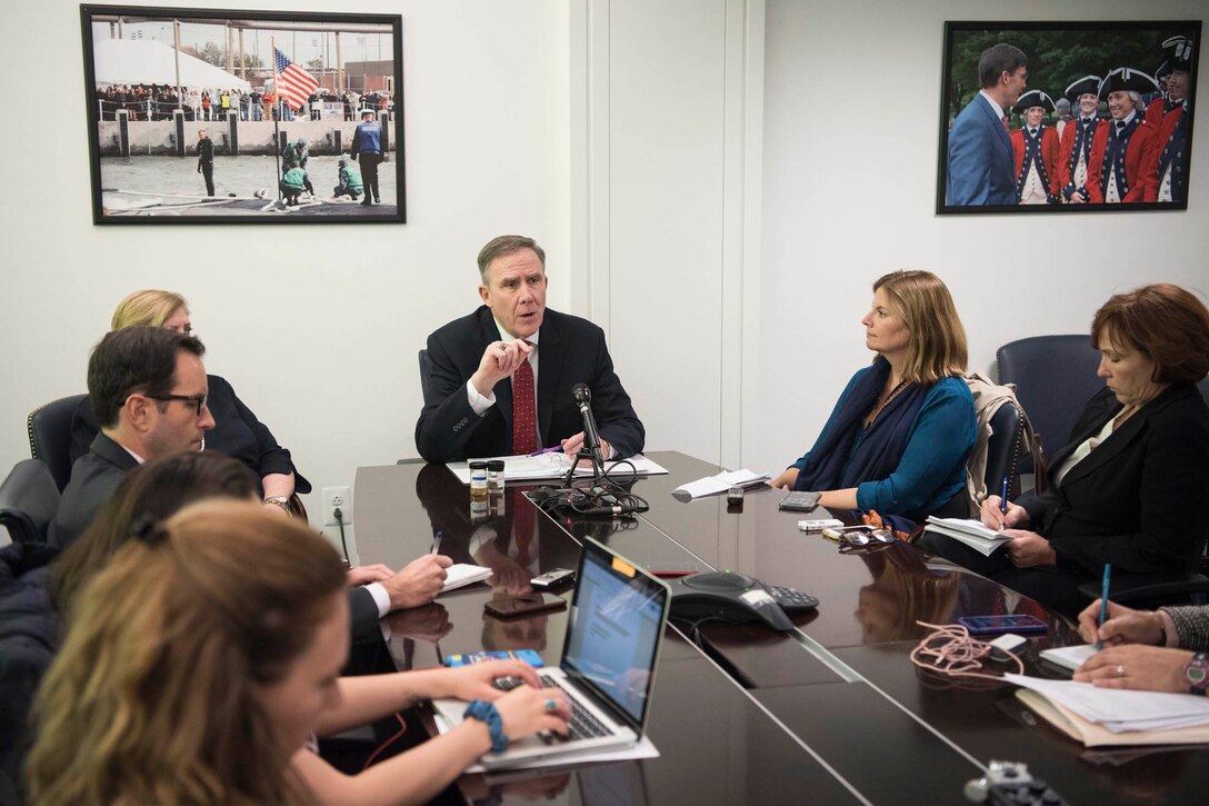 A man speaks to a group of people while sitting at a table.