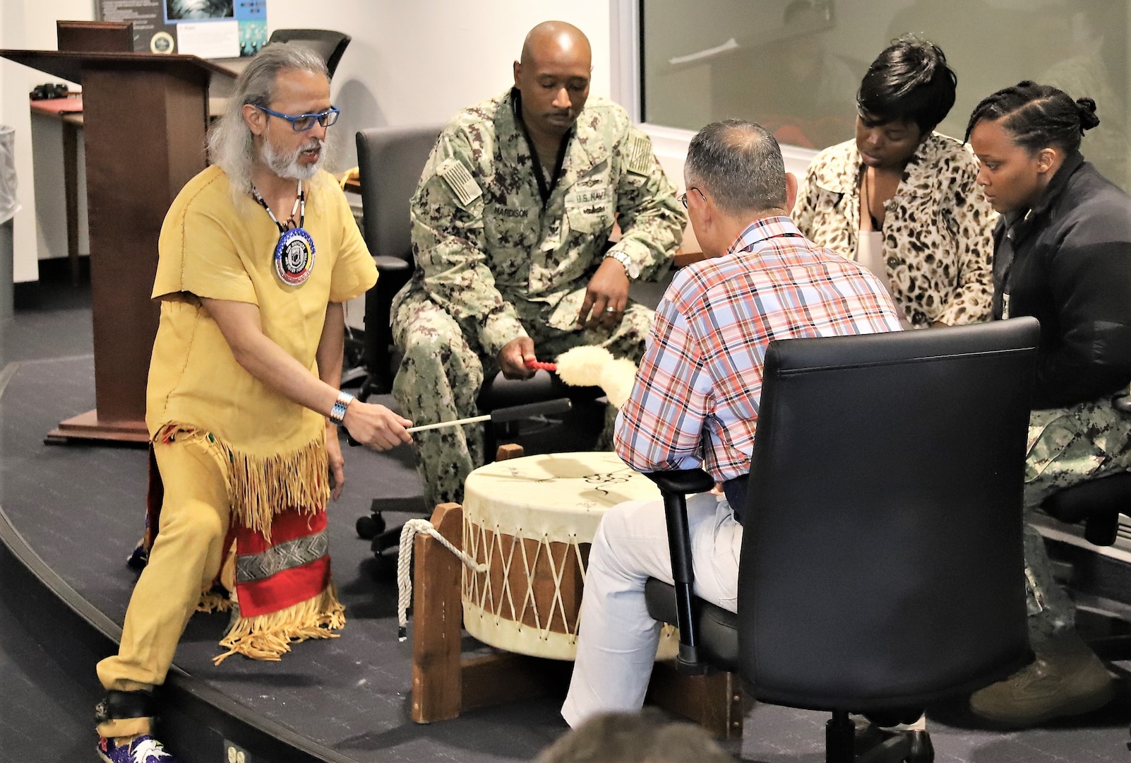 IMAGE: Virginia Beach, Va. (Nov. 12, 2019) – Joe Rubye, a retired Navy chief petty officer and member of the Jicarilla Apache (Tinde) Nation, sings a pow wow song while four Naval Surface Warfare Dahlgren Division - Dam Neck Activity team members keep a rhythmic beat during an American Indian Heritage Month celebration in Hopper Hall Auditorium. Rubye's drum is named “Four Itsa Feather” (Itsa=Eagle) and it is a family heirloom.  (U.S. Navy Photo by IT1 Justin Owens/Released)