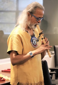 IMAGE: Virginia Beach, Va. (Nov. 12, 2019) – Joe Rubye, a retired Navy chief petty officer and member of the Jicarilla Apache (Tinde) Nation, plays a tribal tune on his flute for Naval Surface Warfare Dahlgren Division - Dam Neck Activity team members during an American Indian Heritage Month celebration in Hopper Hall Auditorium.  (U.S. Navy Photo by George Bieber/Released)