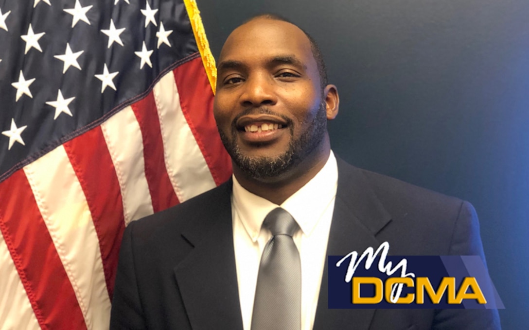 Smiling man wearing a navy blue suit stands beside the American flag