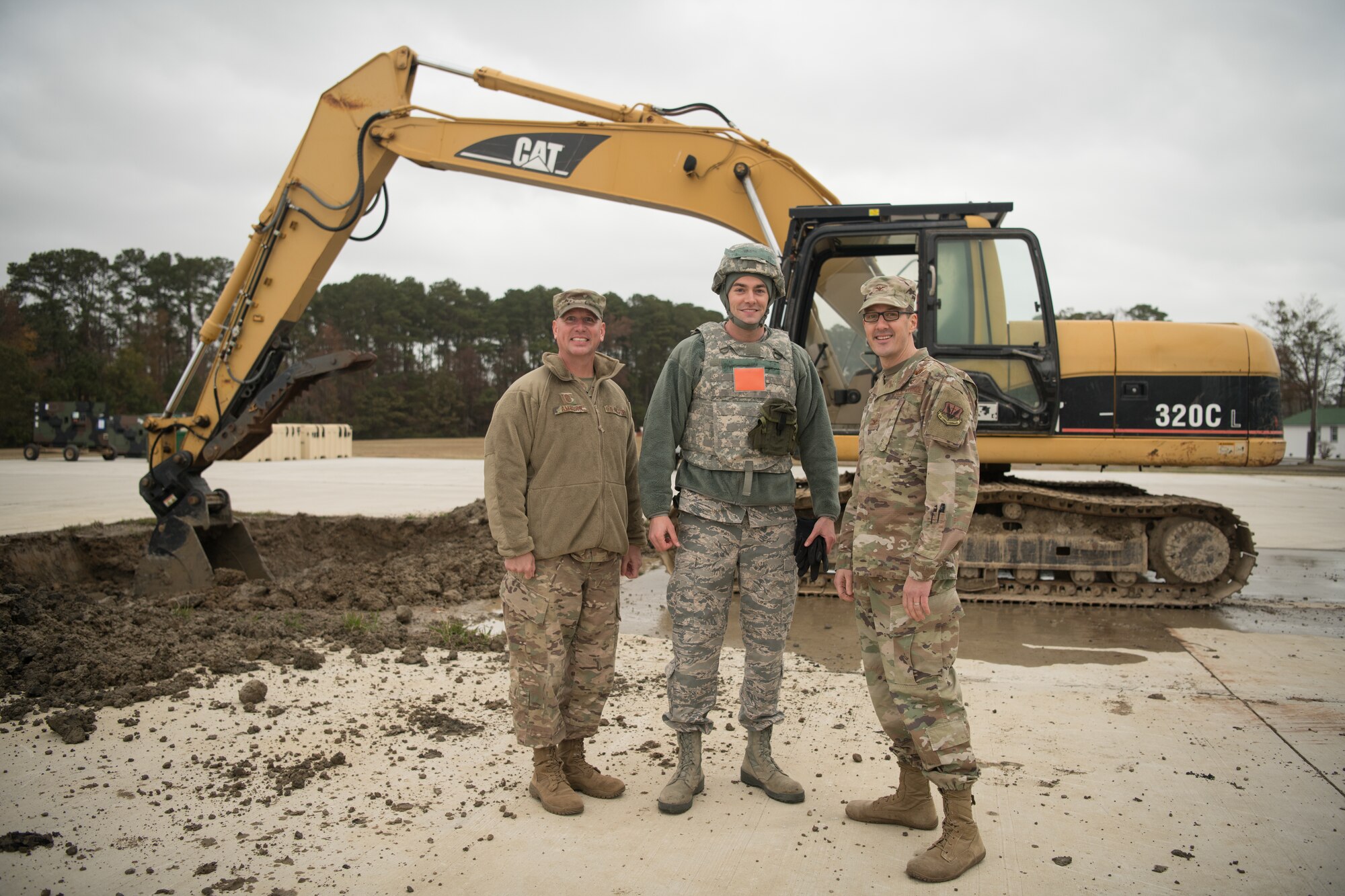 Airmen pose in front of a backhoe