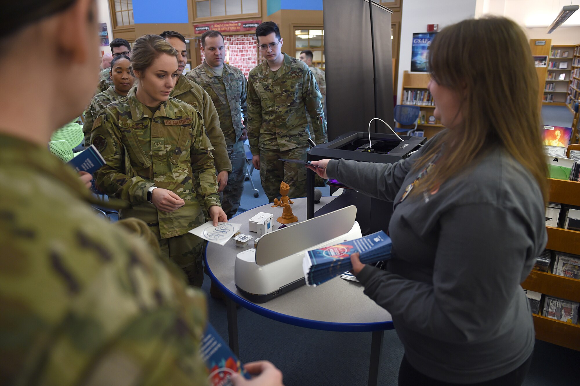 Jessica Muschek, McChord Field Library technician, hands out pamphlets to Airmen participating in Wingman Day as they observe a 3-D printer demonstration at the McChord Field Library, Nov. 15, 2019. Wingman Day offered a variety of classes to Airmen including one on what resources the library offers besides books.
