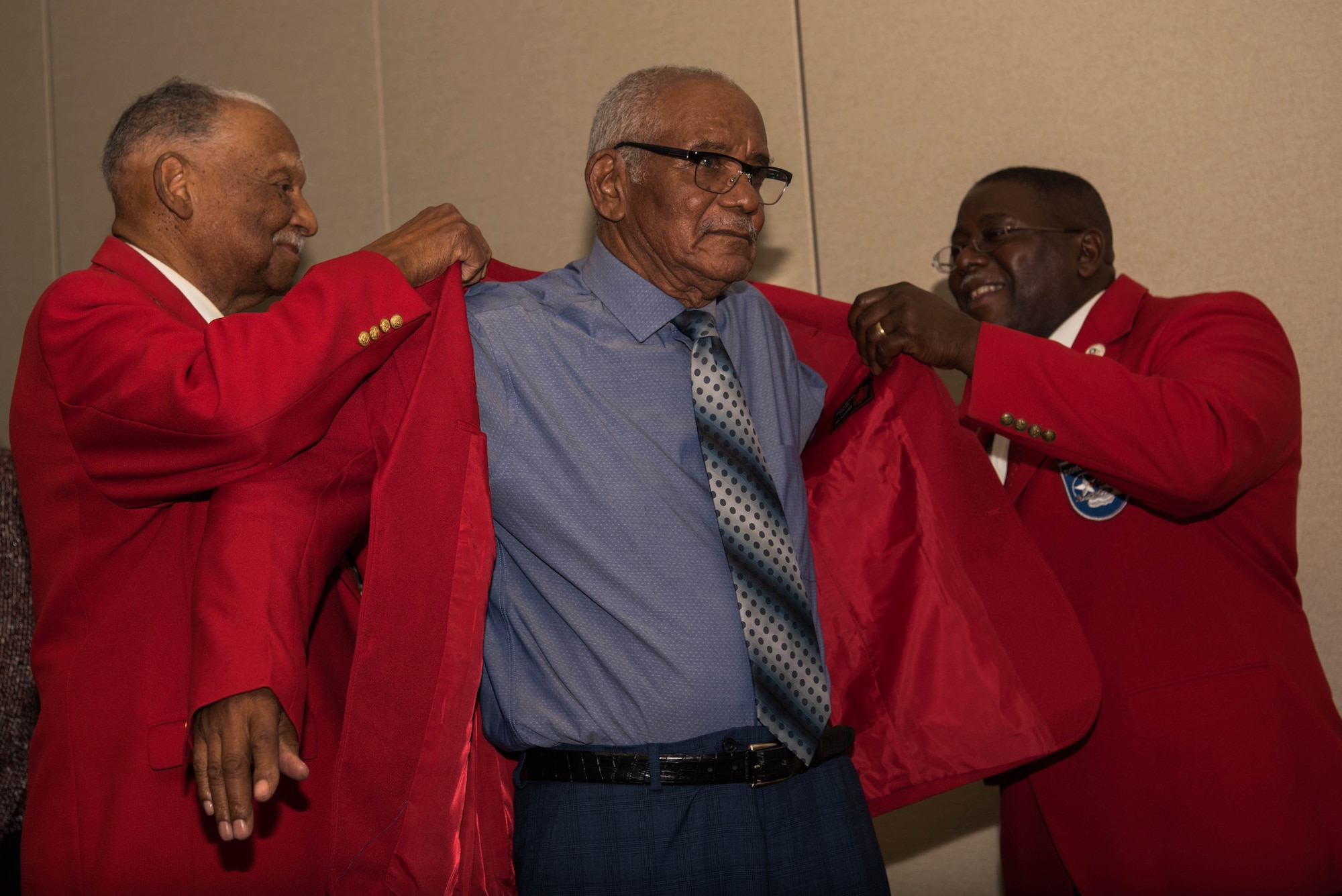 Dr. Harry Quinton, Documented Original Tuskegee Airman (DOTA), and Dr. Bill Burrell, president of the Tidewater Chapter of the Tuskegee Airmen, place the coveted red jacket onto U.S. Army Air Forces Sgt. Thomas Newton, DOTA, during a recognition ceremony in Hampton, Virginia, Nov. 13, 2019. The red jackets are worn to symbolize the “Red Tails,” the nickname the Tuskegee Airmen received during World War II. (U.S. Air Force photo by Airman 1st Class Marcus M. Bullock)