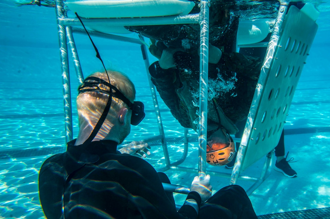 A Marine upside down in a pool with another Marine beside.