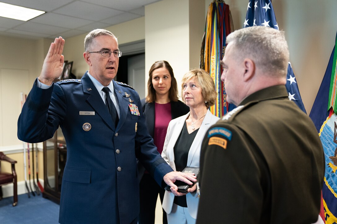 Air Force Gen. John E. Hyten stands and raises his right hand and faces Army Gen. Mark A. Milley