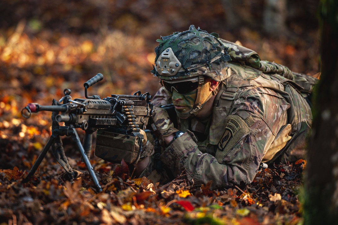 A soldier laying on the ground with a weapon scans an area.