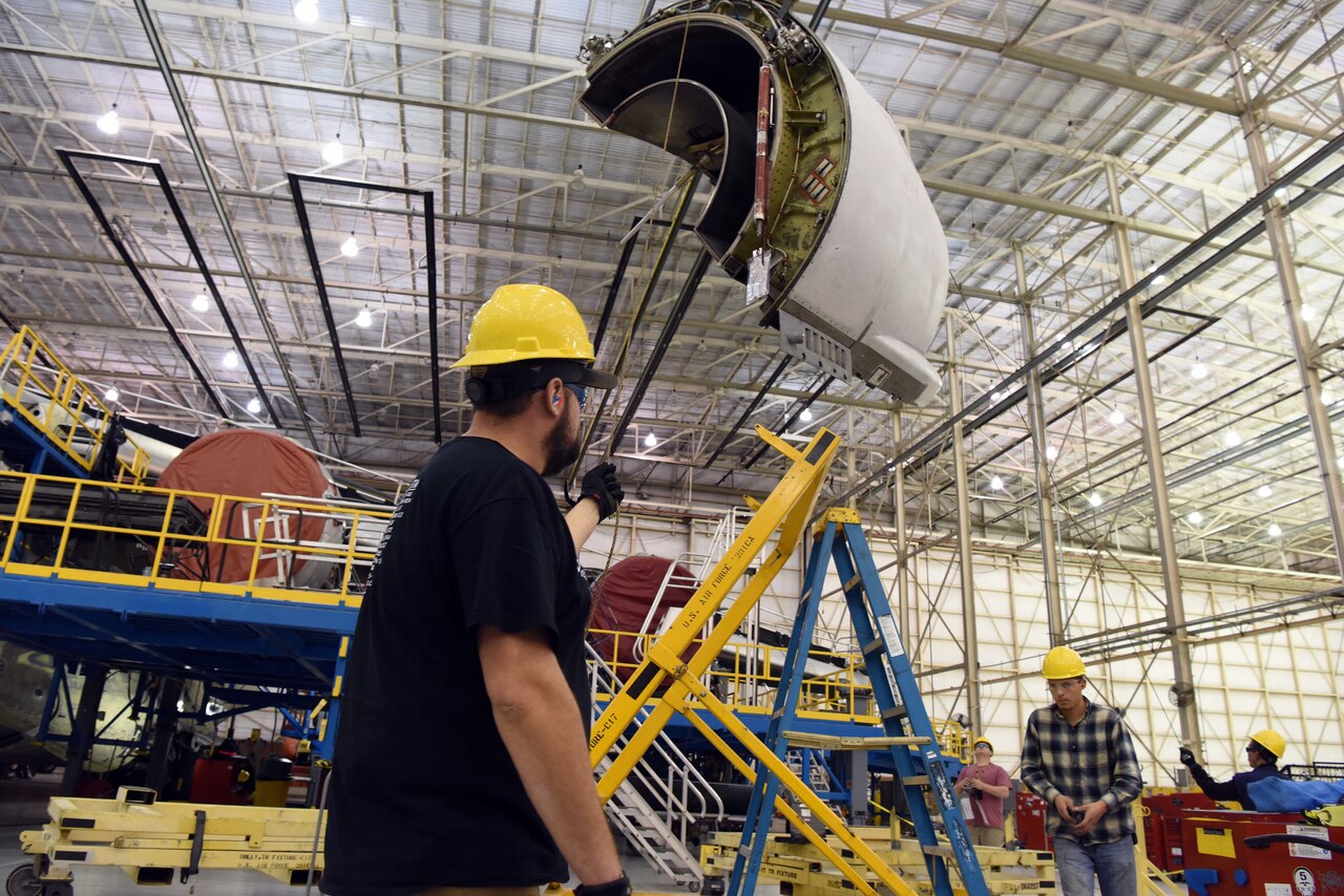 Men personnel work on aircraft in hangar.