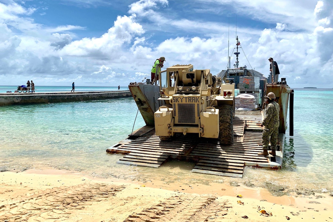 Personnel work on small boat on a beach.